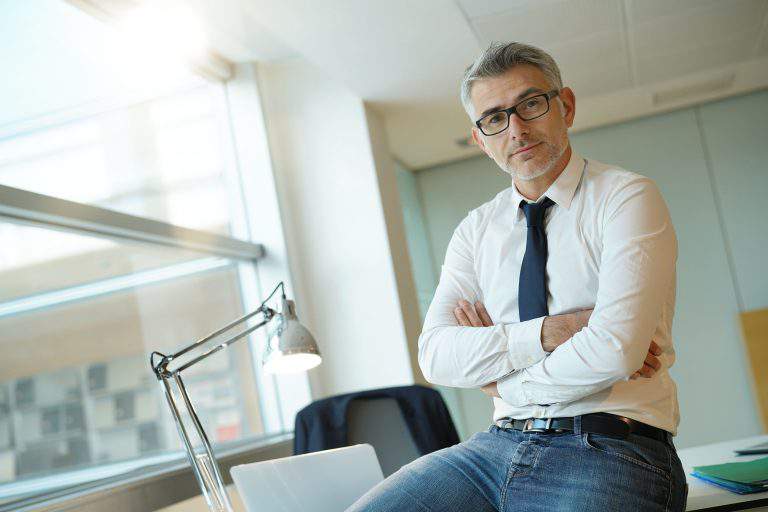 Confident businessman sitting on desk with arms crossed