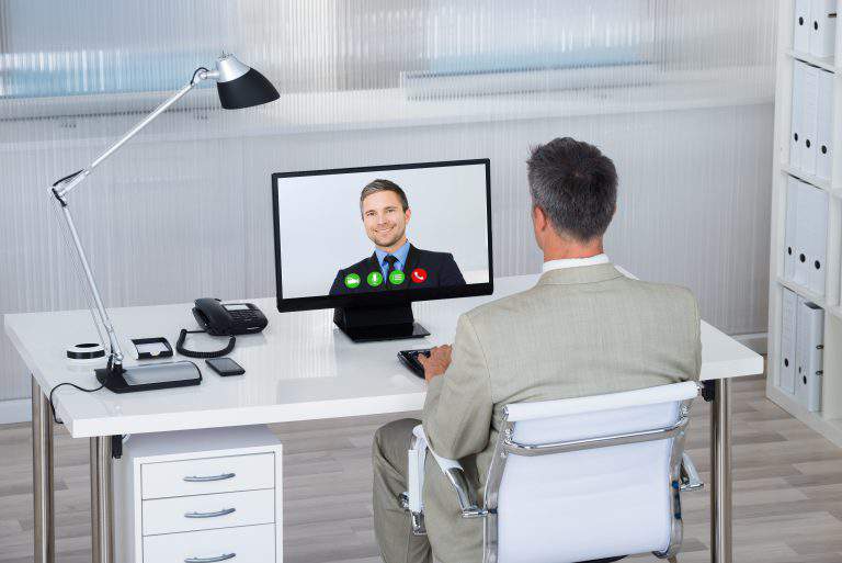 Rear view of businessman video conferencing with partner on computer at desk in office