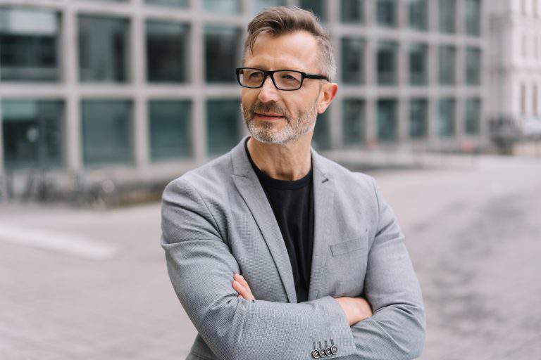 A mature, well dressed, metro man with arms folded in an urban street scene.