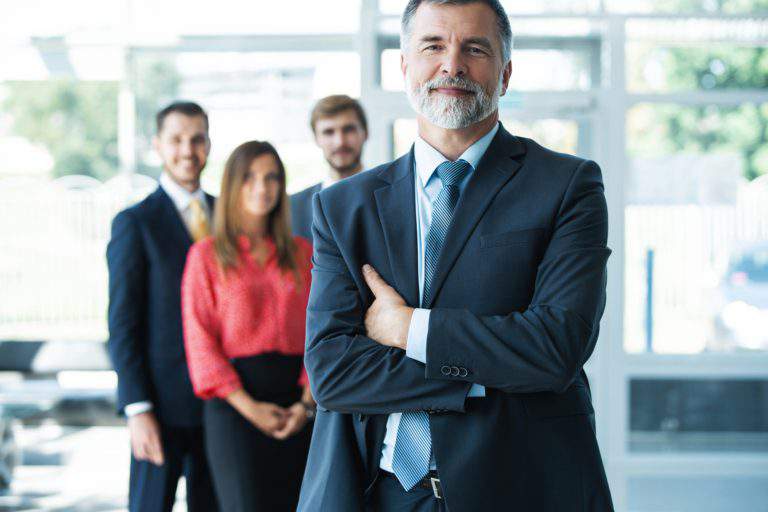 Proud smiling businessman standing with his colleagues at office