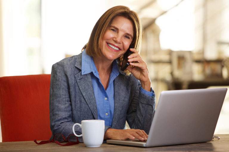 smiling business woman sitting at desk with phone and laptop